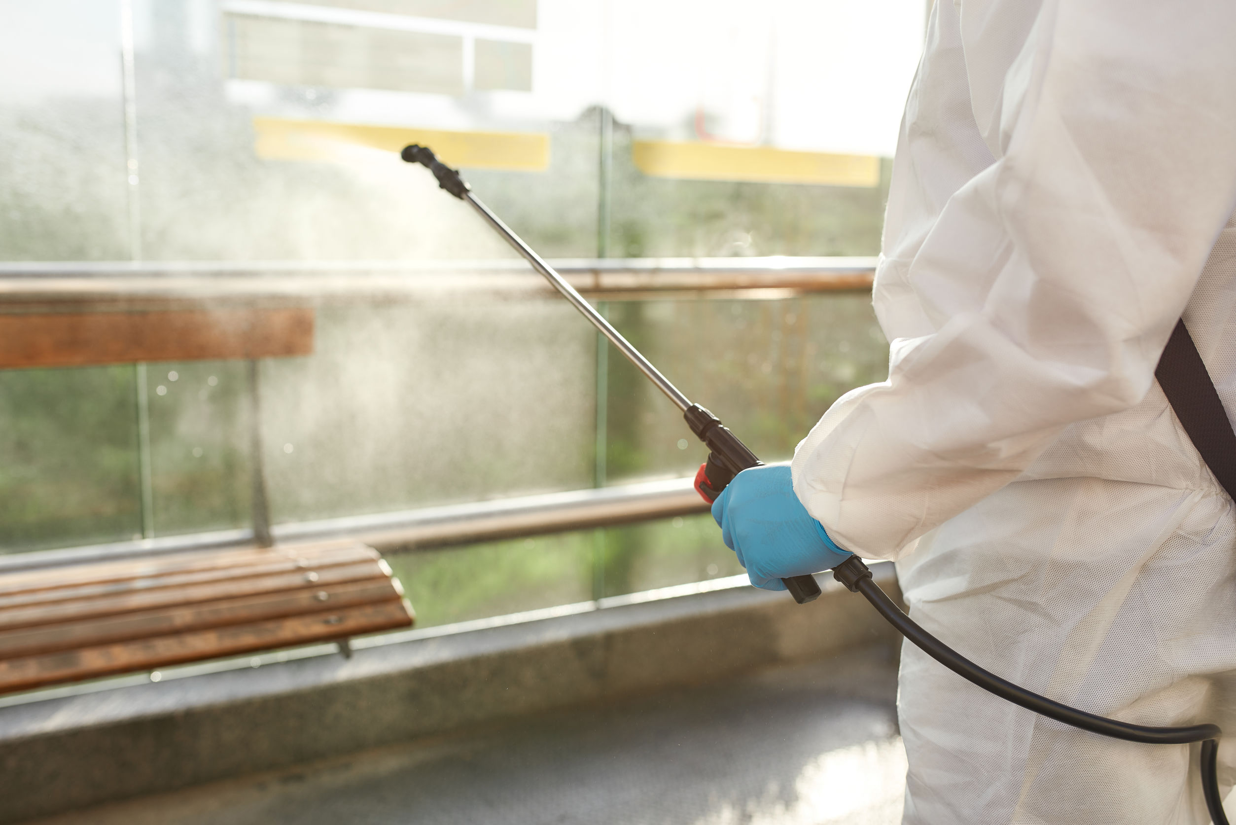 Close up of sanitization, cleaning and disinfection of the city due to the emergence of the Covid19 virus. Man in protective suit at work near the bus stop. Horizontal shot